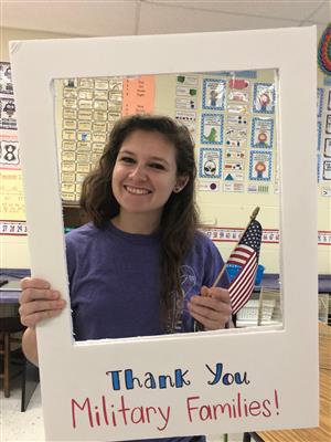 teacher holding flag and thank you sign to military families 